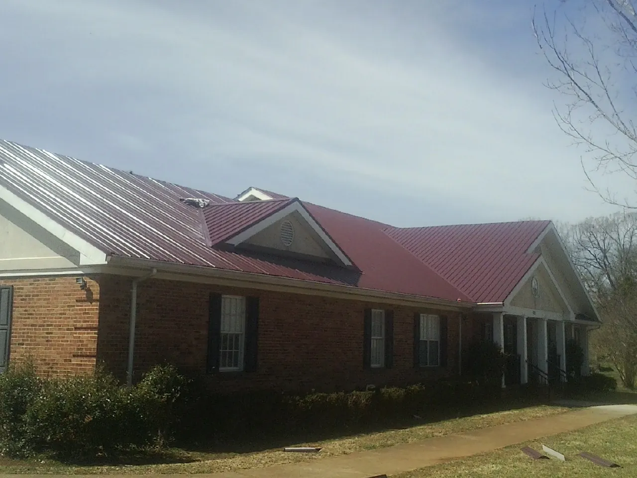 Red metal roof with gabled entries on a long brick building, from a Hail Damage Roof Repair job in Klamath Falls