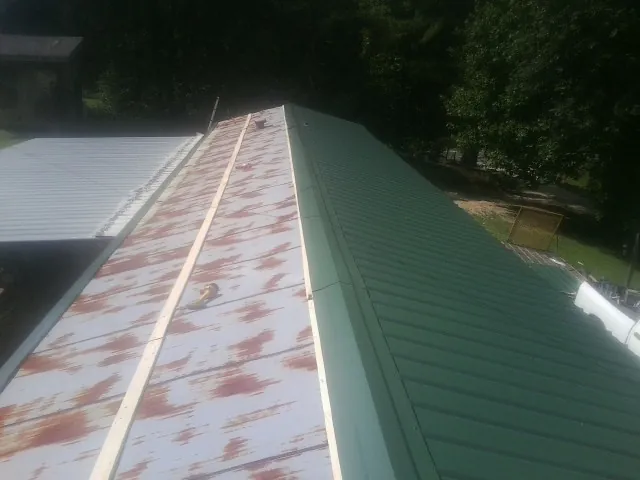 Old rusted panels beside newly installed green metal roofing — Wind Damage Roof Repair by Roofing Brothers in Klamath Falls