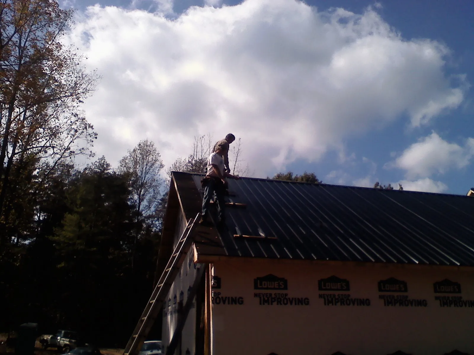 Roofer fastening dark metal panels high against a cloudy sky, from a Roof Inspection job in Klamath Falls