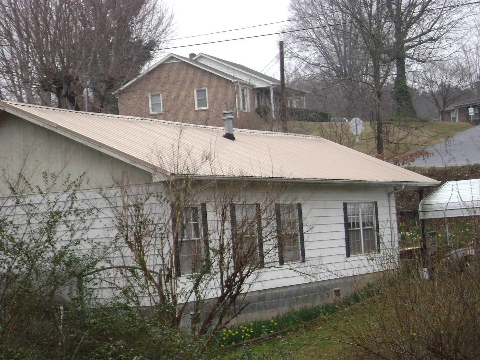Tan metal roof on a white sided house set into a hillside — Commercial Roofing by Roofing Brothers in Klamath Falls